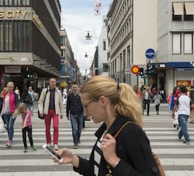 Stockholm, Sweden - June 23, 2015: Pedestrians cross Klarabergsgatan Street in Stockholm, Sweden. In the foreground a woman walks past while looking at her smartphone.