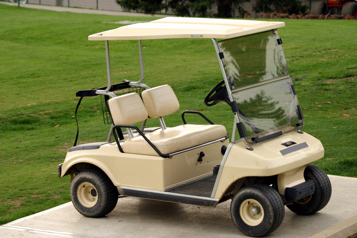 Vintage beige golf cart on a green course representing older models that may contain asbestos in brake components
