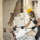 Contractor wearing a respirator and safety gear demolishing a wall during a home renovation as part of a spring checklist for asbestos awareness.