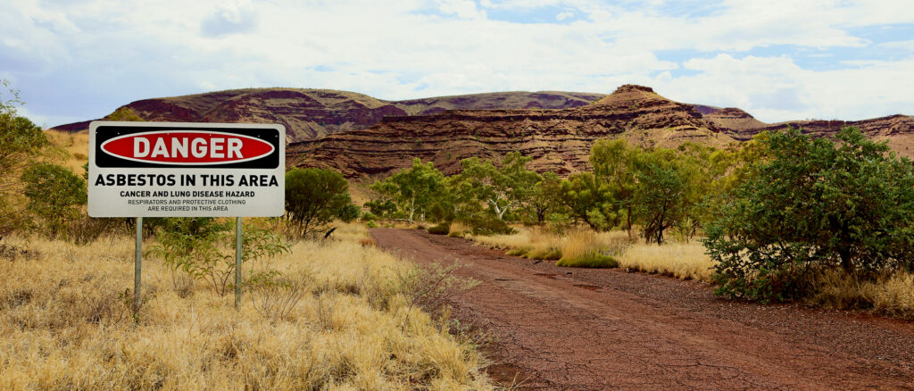 Danger asbestos warning sign at an outdoor mine site with rocky landscape in the background