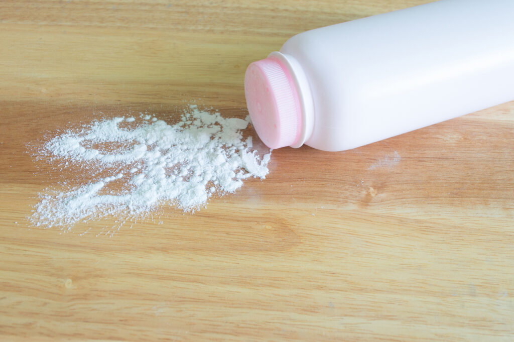 White talcum powder bottle tipped over with powder spilled across a wooden surface