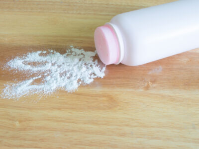 White talcum powder bottle tipped over with powder spilled across a wooden surface