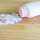 White talcum powder bottle tipped over with powder spilled across a wooden surface
