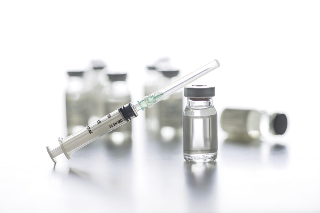 Clear glass vaccine vials and a capped syringe on a white background