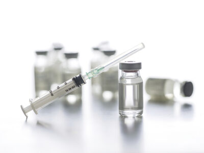 Clear glass vaccine vials and a capped syringe on a white background