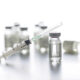 Clear glass vaccine vials and a capped syringe on a white background